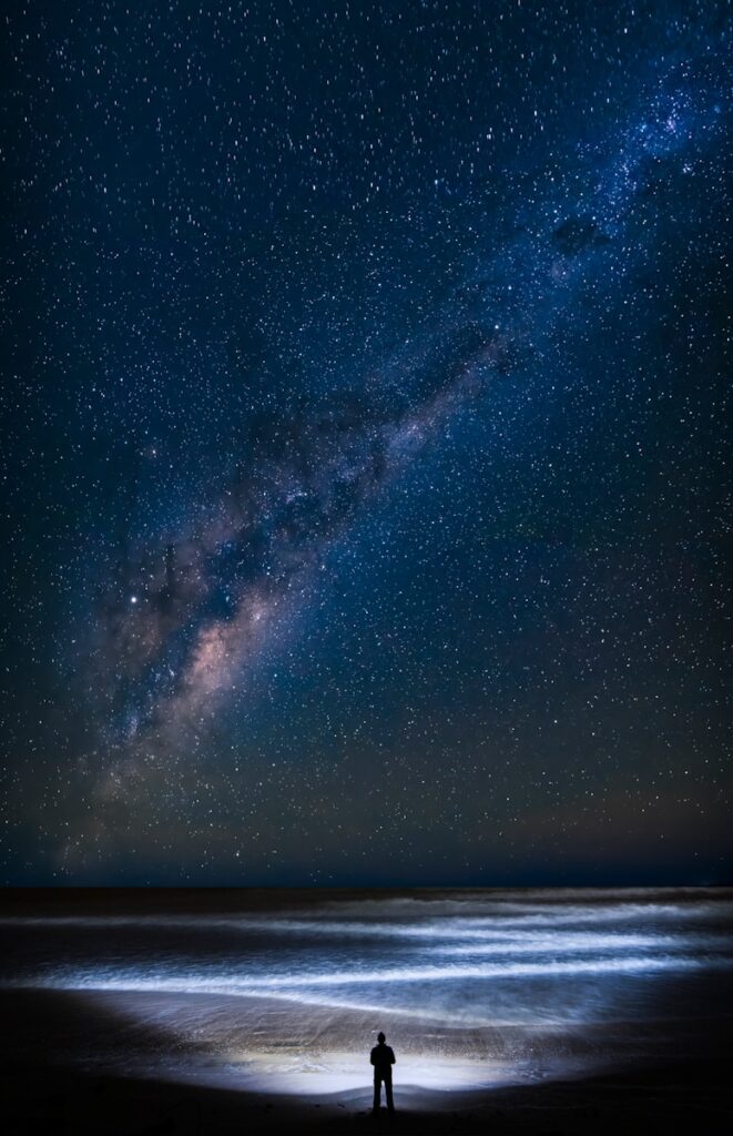 a man standing on top of a beach under a night sky