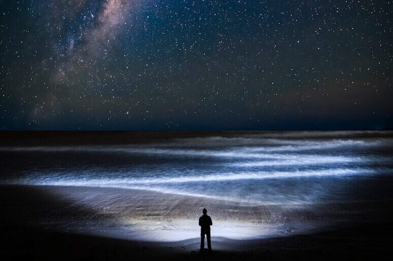 a man standing on top of a beach under a night sky